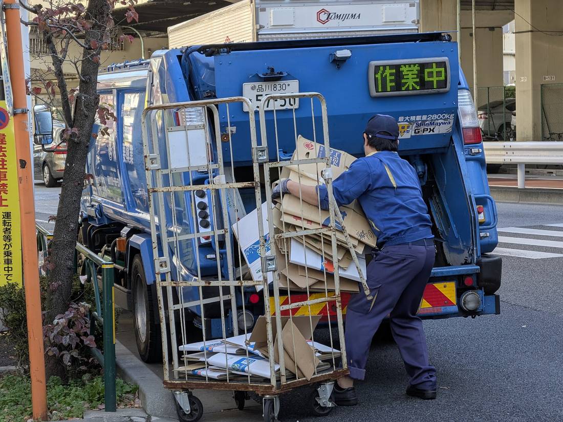 ごみ収集車の後部投入口に段ボールを積み込む作業員