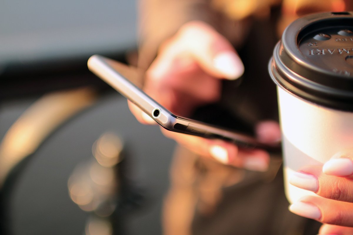 コーヒーを手にスマートフォンを操作する人の手元