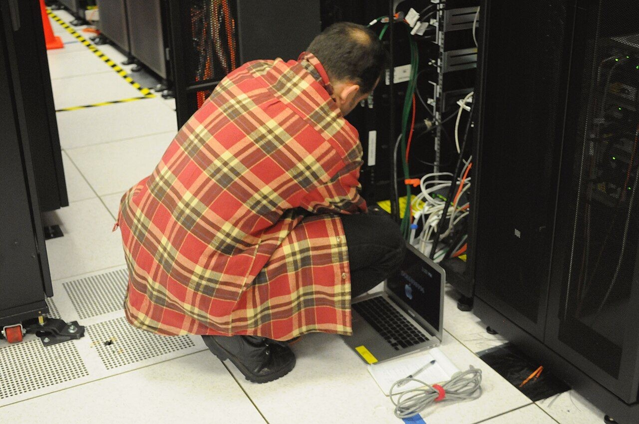 データセンターでサーバーラックの前にしゃがみ、ノートパソコンで作業する技術者